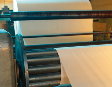 Een grote folierol die door de rollen van een industriële slitmachine wordt geleid.